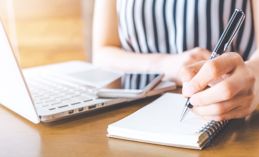 Business woman hand working at a computer and writing on a noteped