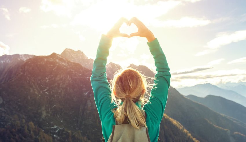 Young woman on mountain top makes heart shape finger frame