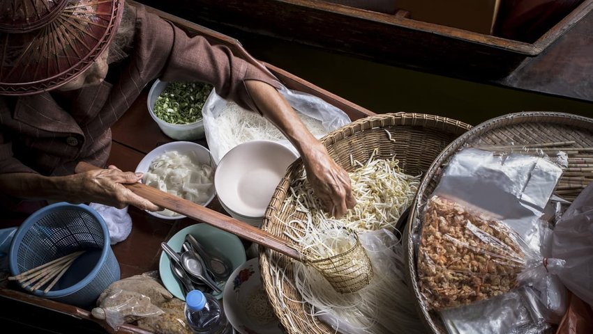 Old woman making thai noodle food in local floating boat market