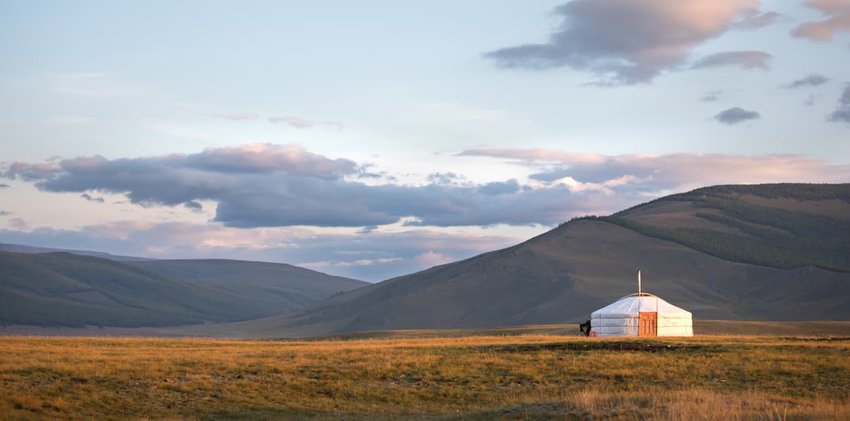 Traditional Mongolian ger on a mountain backdrop in sunset light