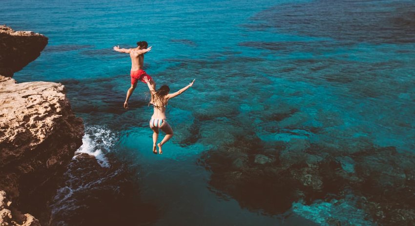 Young brave divers couple jumping off cliff into ocean