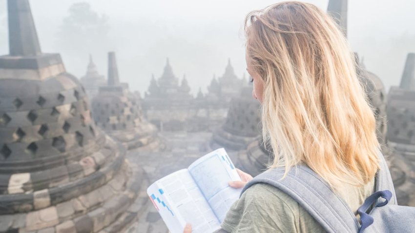 Girl with guide book observes sunrise at Borobudur temple, Indonesia