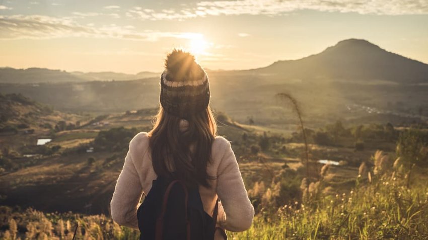 young woman traveler watching the sunrise over mountains