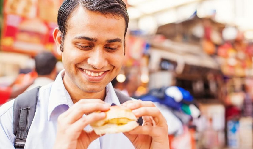 young indian man eating veda pav on the street