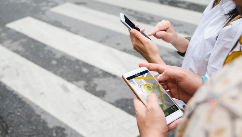 Photo of two people using their phones with a crosswalk in the background