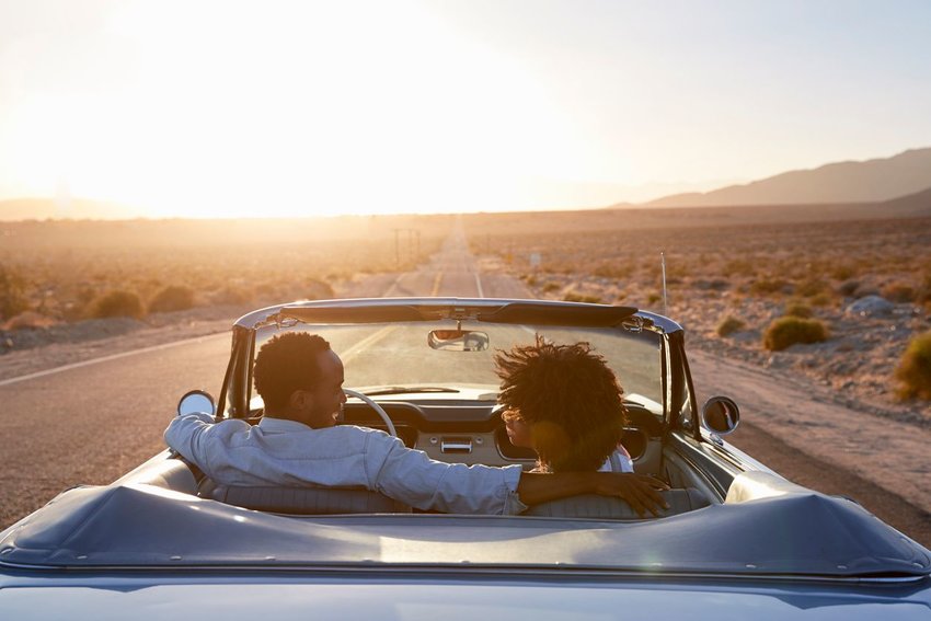 Photo of a couple in a convertible, driving on an open road