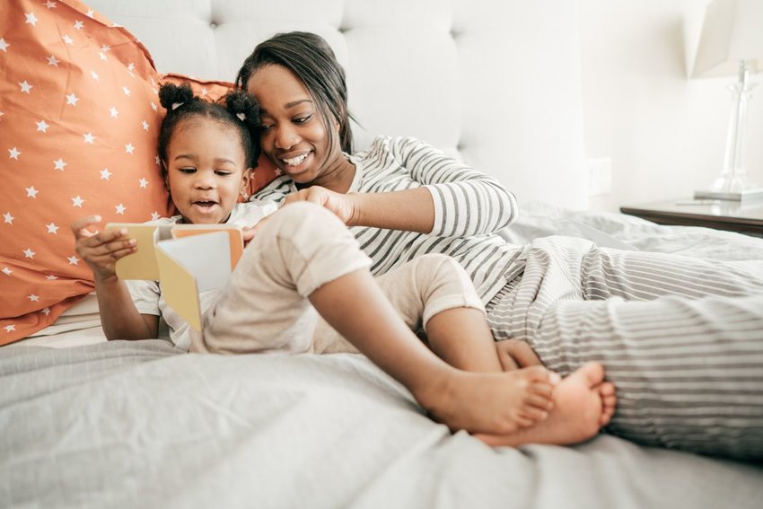 Photo of mom and young daughter reading in bed