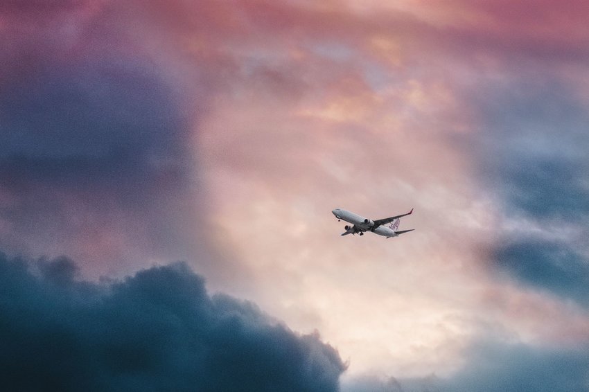 Plane flying through a break in clouds at sunrise