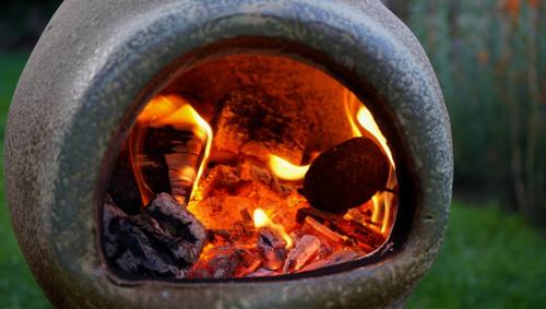 Close up of a Chiminea on fire in a garden.