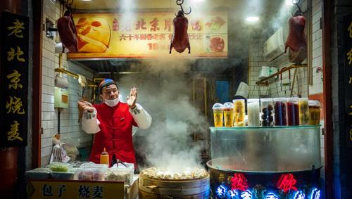 Chinese vendor of Wangfujing street food market selling Beijing duck and Baozi at night.