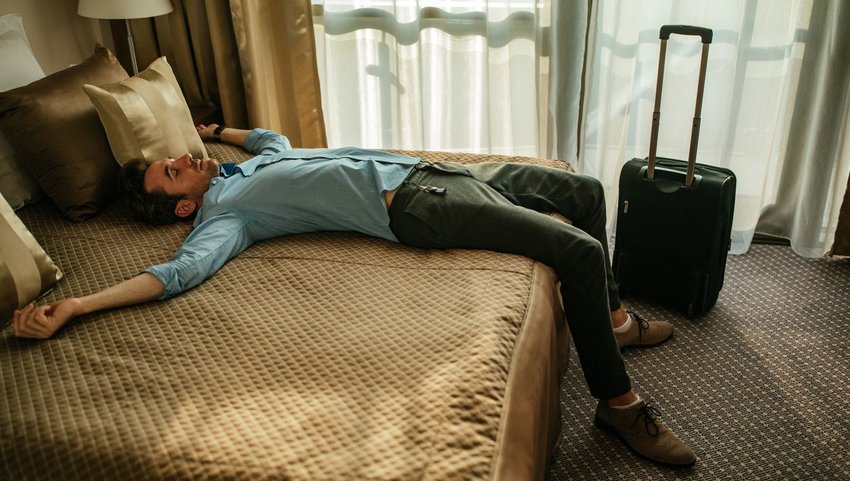 Man asleep on a hotel bed in daytime clothes and shoes