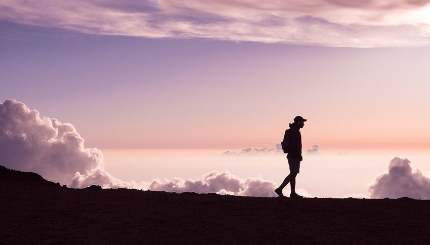 Man walking on a mountain ridge at sunrise with clouds in the background