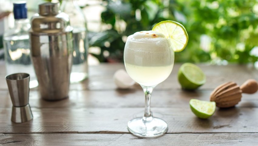 Front view of Pisco Sour cocktail on table with limes and shaker