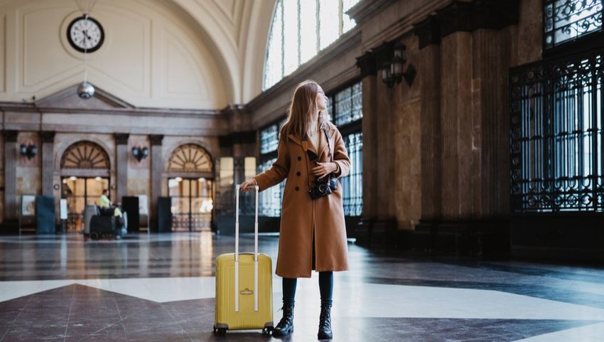 Woman in trench coat and boots with bright yellow suitcase