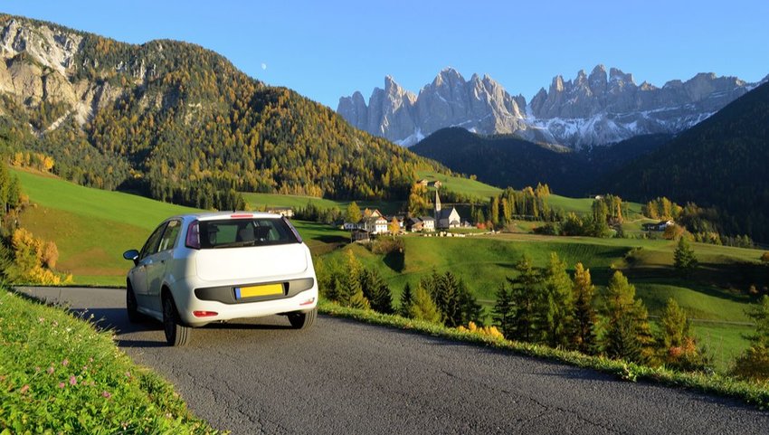 White car in autumn driving through the Funes Valley in the Dolomites, South Tyrol, Italy 