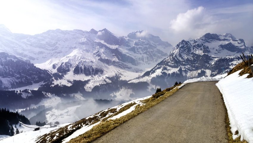 Narrow road in the Swiss Alps overlooking snow covered mountains