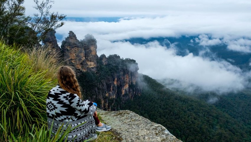Woman relaxing on cliff overlooking the Three Sisters Rocks, Katoomba, New South Wales, Australia