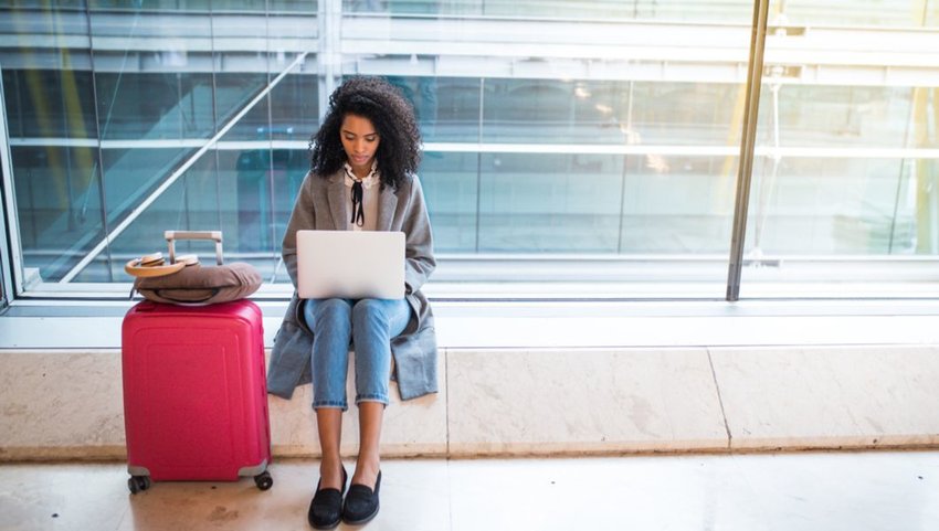 Woman with large suitcase working on laptop in airport terminal