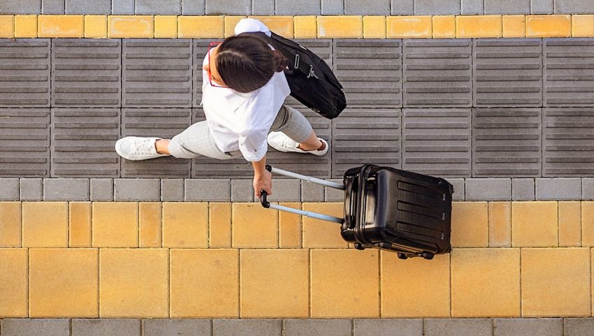 young woman walking on a sidewalk and pulling a small wheeled luggage