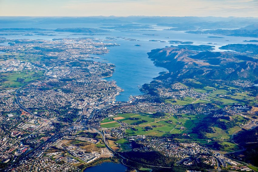 Aerial view of city on water with mountains in background.