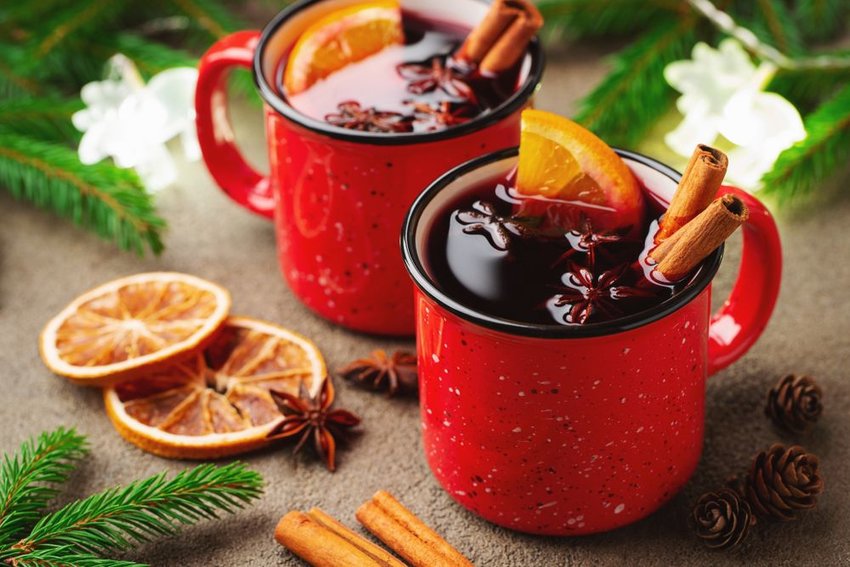 Two red mugs of glühwein with orange slices and cinnamon sticks