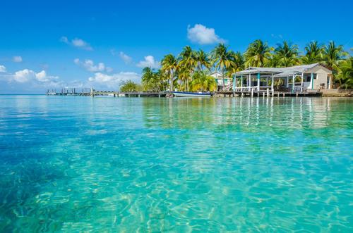 Clear blue water with homes on shore with palm trees in Belize Cayes