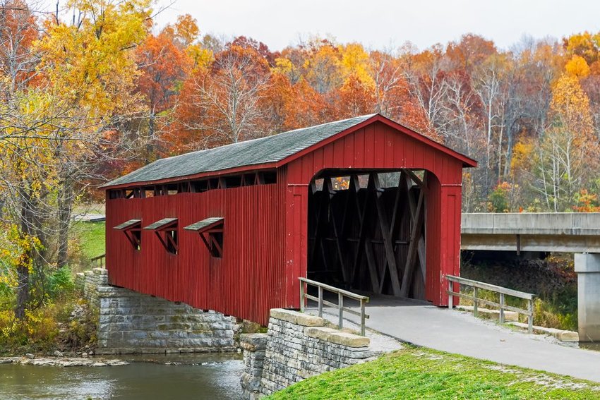 The historic red Cataract Covered Bridge crosses Indiana's Mill Creek with fall trees 