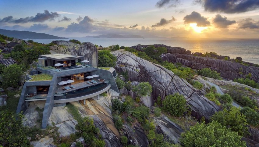 Hotel on rocky hill with ocean in background at sunset