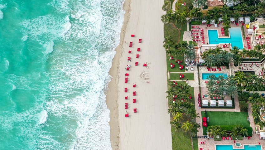Aerial view of beach lines with red lounge chairs and hotel pools 