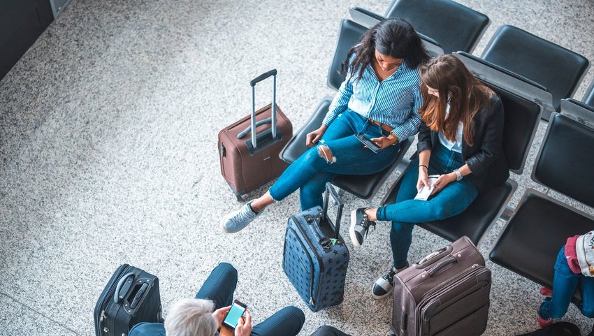 Two women looking at phone while sitting in airport chairs surrounded by luggage