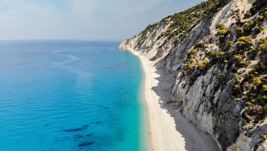 Aerial view of long narrow beach against cliff and bright blue waters