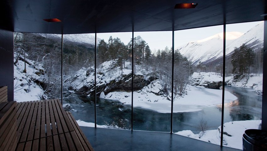 Large floor to ceiling windows in a spa with views of a river and mountainous landscape covered in snow