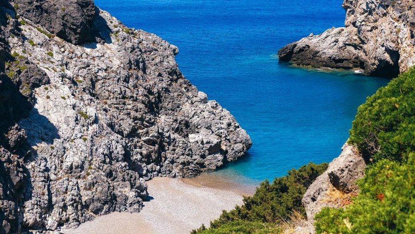 Hidden beach surrounded by rocks leading into deep blue water