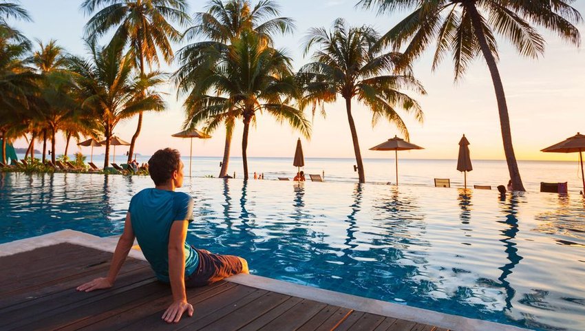 Person sitting on side of pool with feet in water, looking off into sunset