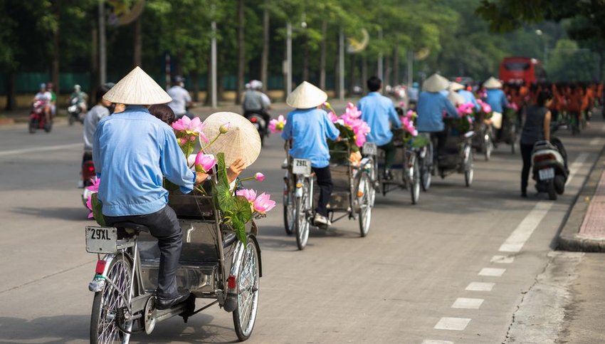 Cyclo drivers wearing hats on Hanoi street with passengers