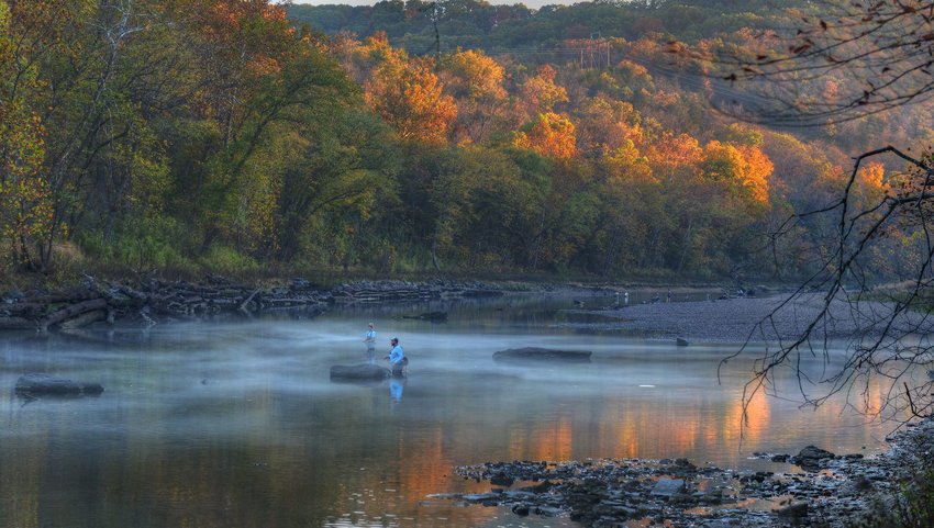 Two people fishing in a river with fall colored trees