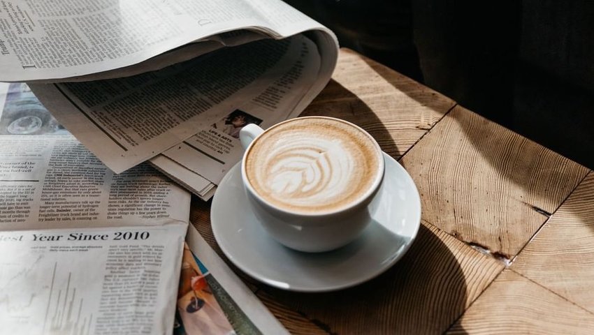 Mug of coffee on wooden table with newspapers