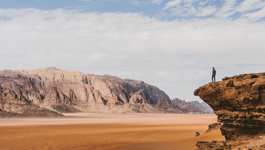 Person standing on rock ledge with rocky mountains in the background 