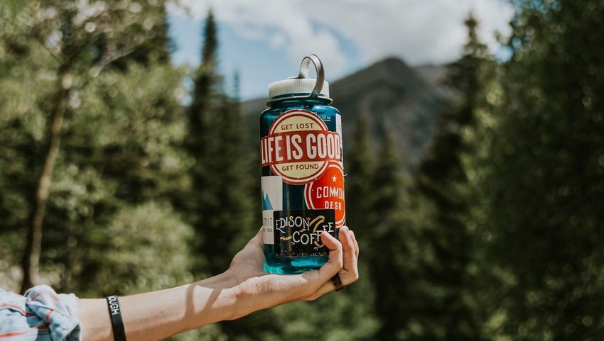 Person holding up a water bottle with stickers on it and trees in the background