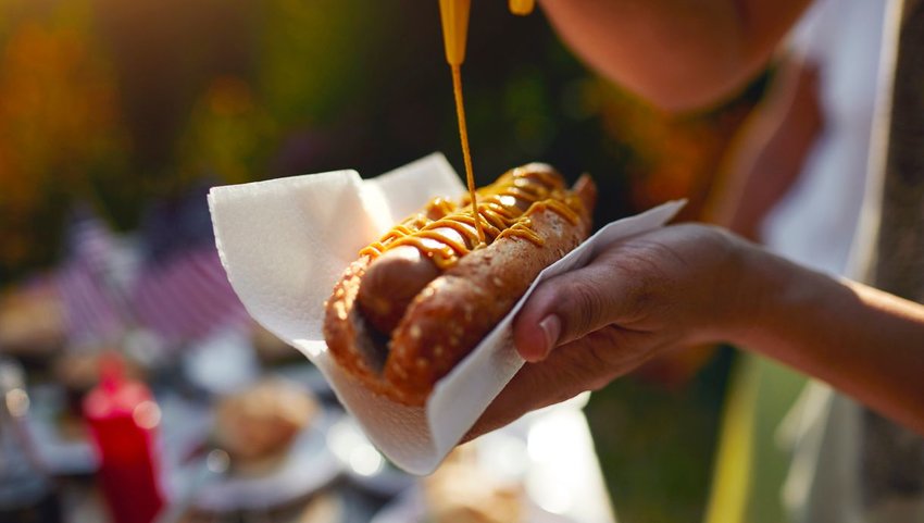 Person holding a hotdog while putting on mustard 