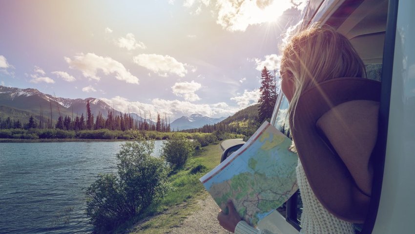 Woman leaning out of car with map looking out at lake and mountains