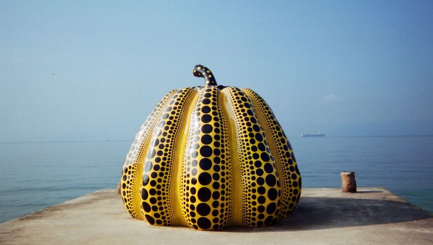 Yellow pumpkin sculpture on end of pier with ocean behind 