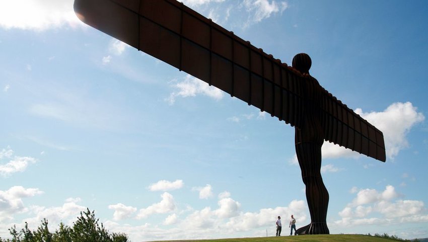 Two people standing at the foot of the Angel of the North, located in Northumberland