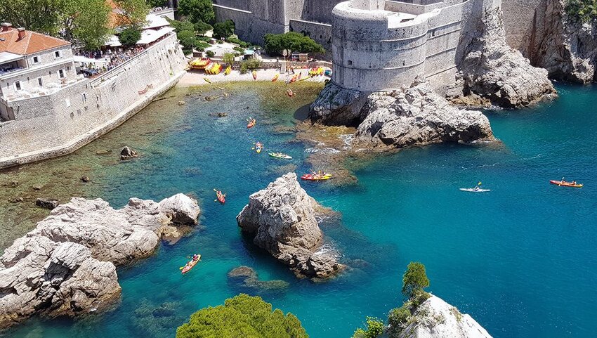 Kayakers along coast with rocks and stone buildings.