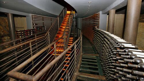 Wine bottles stacked on walls in cellar and staircase in the center. 
