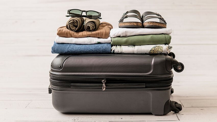 Closed suitcase with folded clothes, sunglasses, and sandals on top.