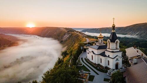 Aerial view of valley with river and fog, monastery located on a hill in Moldova at sunset.