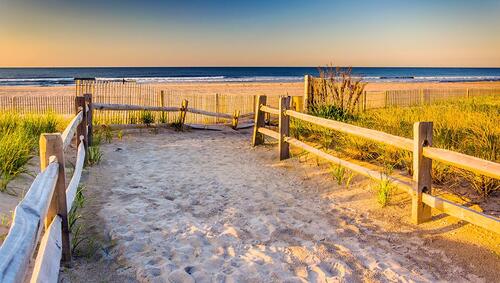 Fenced path over sand dunes with ocean in background. 