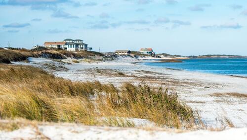 Beach Front Houses at the coast of North Carolina with sand, sea grass and ocean in the foreground.