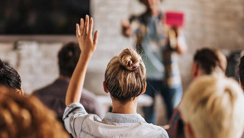 The back of a woman raising her hand in a seminar.
